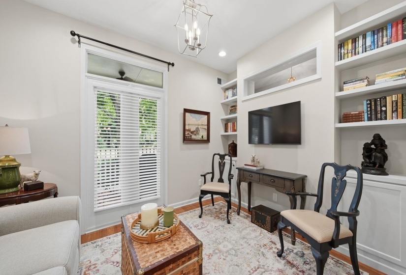 Built-in shelving and cabinetry, wood-finish flooring, overhead lighting, and a large window with blinds