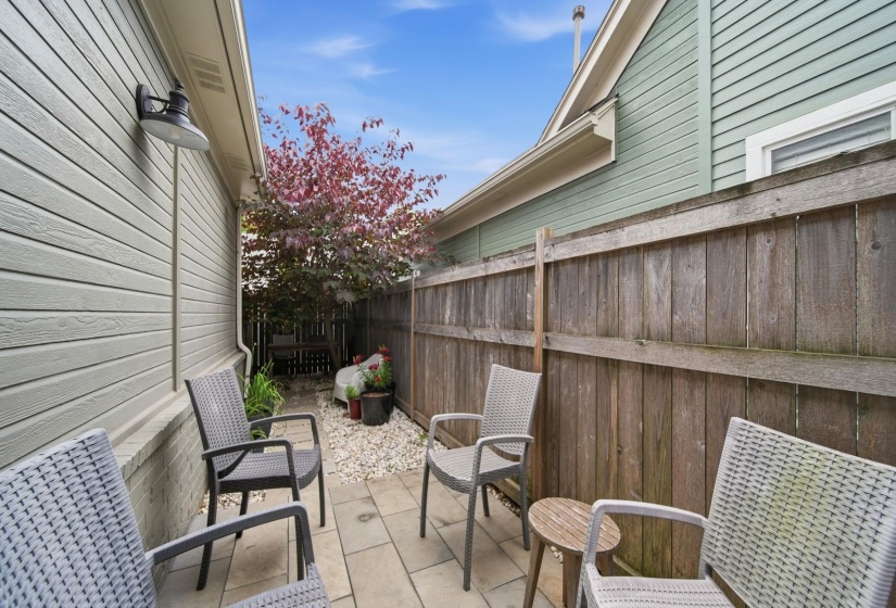 Private patio area featuring paver stones, a wooden privacy fence, and a gravel bed with mature plantings