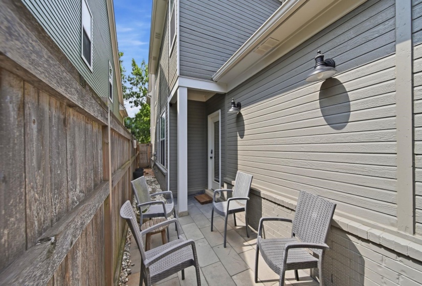 Paved patio area featuring exterior wall lighting fixtures and a wood privacy fence