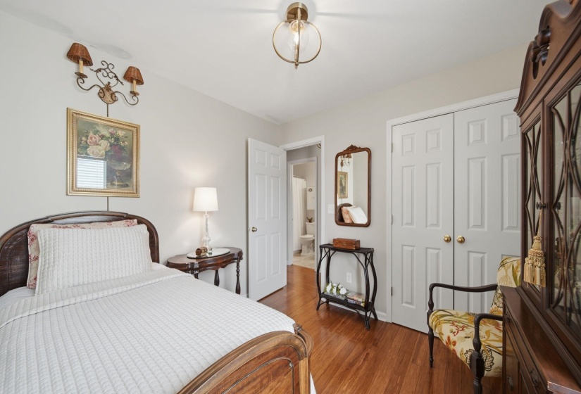 Bedroom featuring wood-finish flooring, white paneled double doors, a built-in wall sconce, and a brass-finish ceiling light fixture