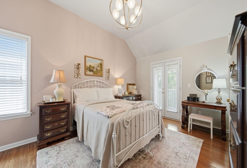Bedroom featuring vaulted ceilings, wood-finish flooring, a ceiling-mounted light fixture, and double glass-paneled doors with blinds