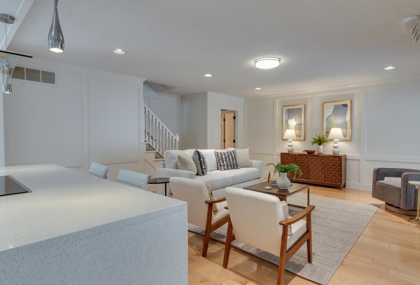 Open-concept living space featuring wood-finish flooring, recessed lighting, a built-in staircase with white risers, and decorative wall paneling
