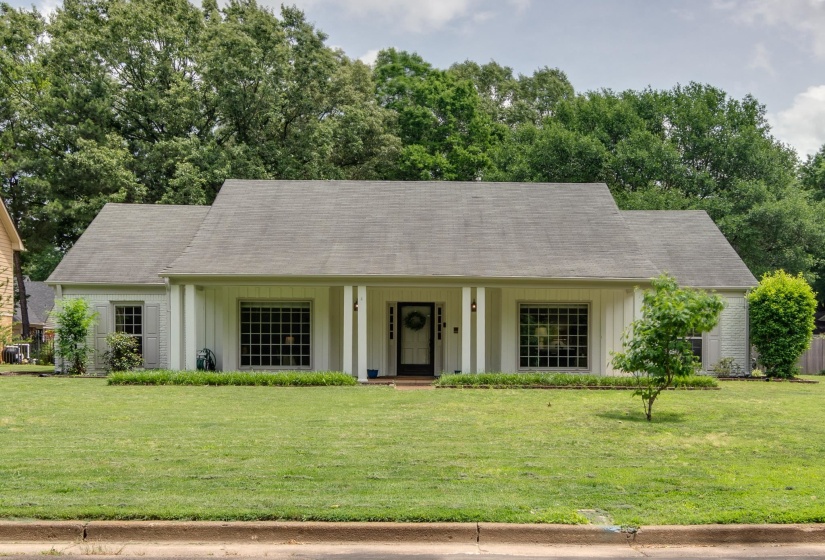 White painted brick exterior with a prominent front lawn, multiple windows with grid patterns, and a covered porch entry