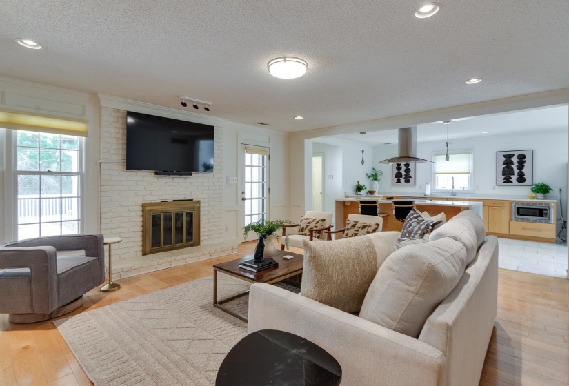 Open-concept living space featuring wood-finish flooring, a white brick fireplace with a brass firebox, and recessed lighting
