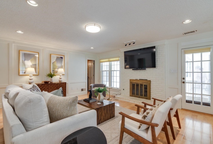 Living space featuring wood-finish flooring, a painted brick fireplace with a wood mantle, and a glass-paneled door