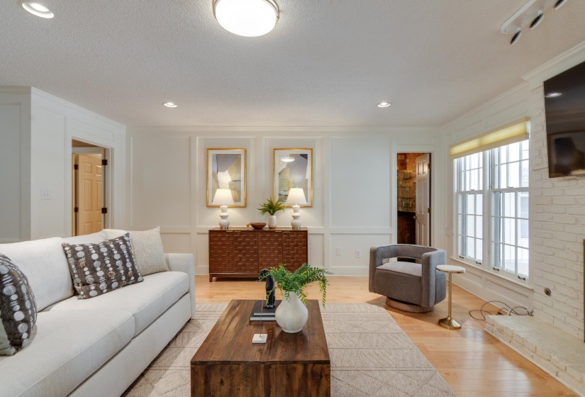 Living area with light wood-finish flooring, white paneled walls, recessed lighting, and a white brick-finish fireplace