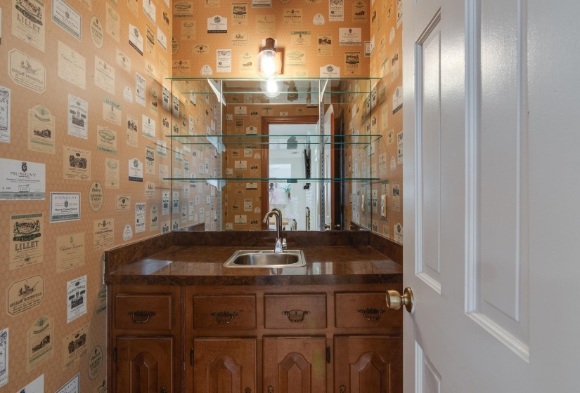 Wet bar featuring a stainless steel sink, dark wood cabinetry with bronze hardware, and a coordinating countertop