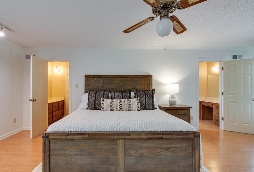 Spacious bedroom featuring light wood-finish flooring, a ceiling fan with integrated lighting, and white walls