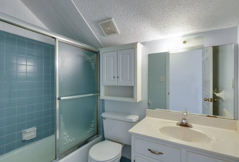 Bathroom featuring a built-in vanity with an integrated sink and mirror, white cabinetry, toilet, and a bathtub with blue tile surround and sliding glass shower door