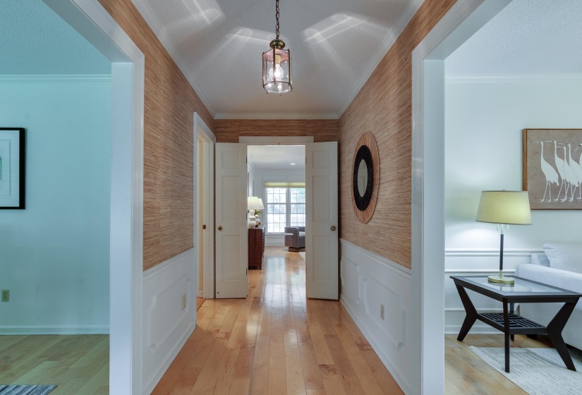 Hardwood flooring extending through a central hallway featuring wainscoting and textured wall covering