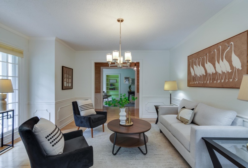 Bright living area featuring crown molding, wainscoting, wood-finish flooring, and a brushed nickel chandelier