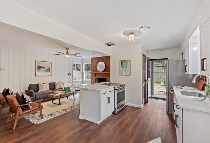 Open-concept living space featuring wood-finish flooring, white cabinetry, stainless steel appliances, and a brick fireplace