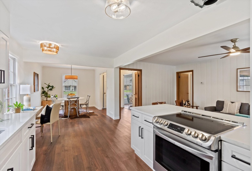 Open-concept living space featuring wood-finish flooring, white cabinetry with dark hardware, a stainless steel electric range, and recessed lighting