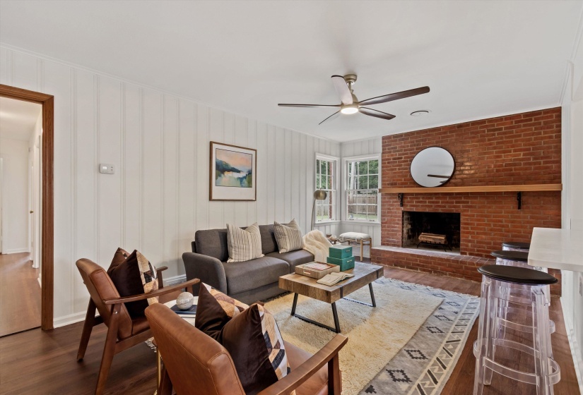 Living area featuring a prominent brick fireplace with a wood mantel, wood-finish flooring, and vertical plank wall paneling
