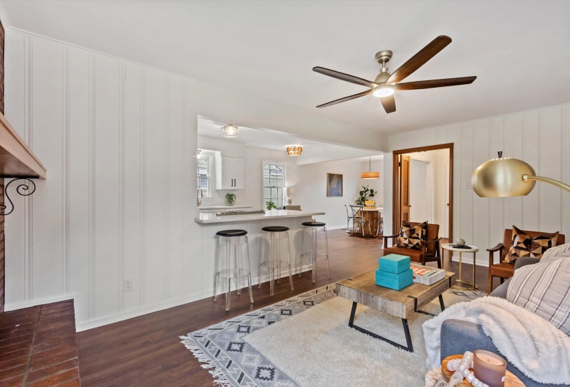 Open-concept living area featuring wood-finish flooring, a contemporary ceiling fan, and a pass-through breakfast bar with a light-toned countertop