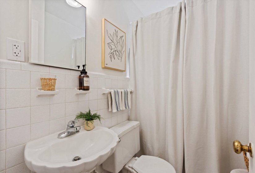 Bathroom featuring white tiled walls, a scalloped pedestal sink with chrome faucet, a wall-mounted mirror, and a full-height shower curtain