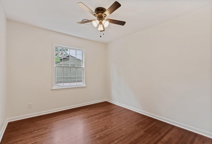 Room featuring wood-finish flooring, a double-hung window, and a ceiling fan with integrated lighting