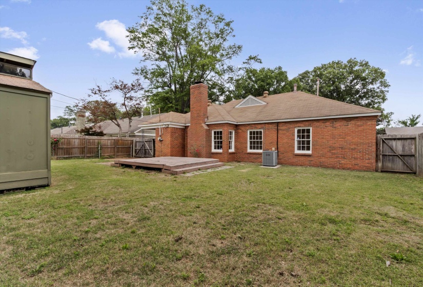 Spacious backyard featuring a multi-level wooden deck, a brick exterior, multiple windows, a prominent brick chimney, and a wooden privacy fence