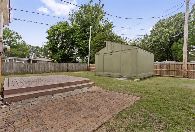 Private backyard featuring a wood deck with two steps, a brick paver patio, a utility shed, and a wood privacy fence