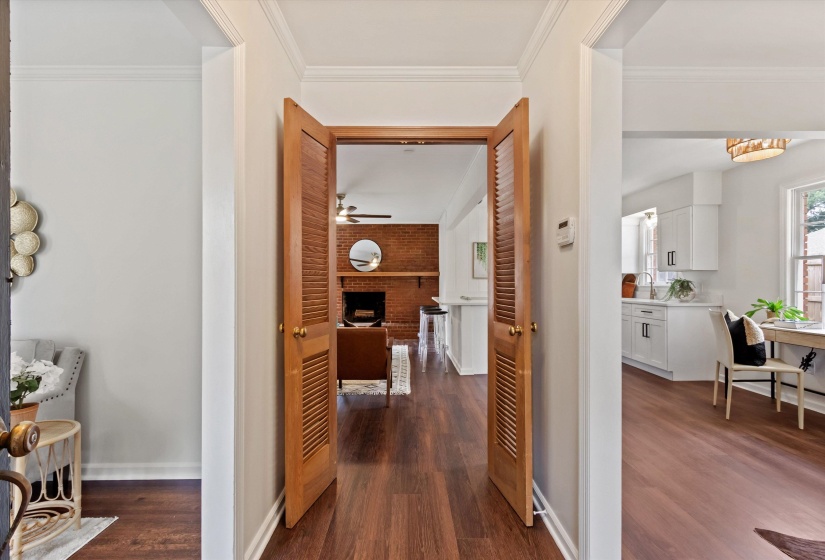 Wood-finish flooring throughout, with a living area featuring a brick fireplace and a kitchen with white cabinetry and a window