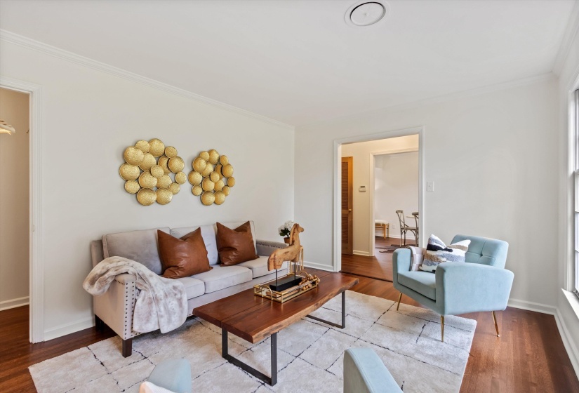 Living area featuring wood-finish flooring, a neutral color palette, crown molding, and an open doorway to another room