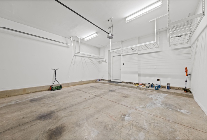 Spacious garage featuring a concrete floor, bright overhead lighting, two built-in overhead storage racks, a wall-mounted slat storage system, and a side access door