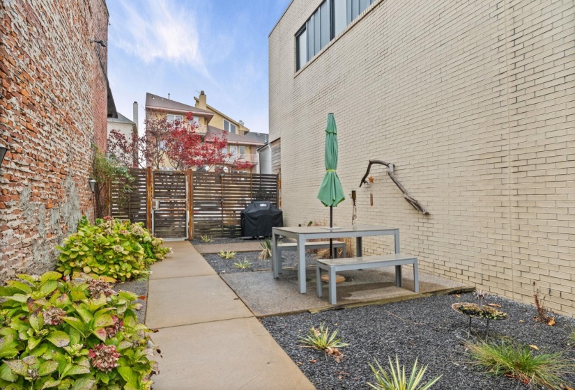 Private outdoor patio featuring a concrete paver path, dark gravel landscaping, mature shrubs, and a slatted privacy fence
