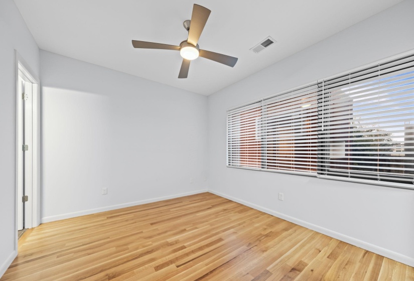 Room featuring wood-finish flooring, a contemporary ceiling fan with integrated lighting, and multiple windows with horizontal blinds