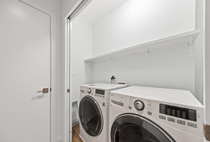 Dedicated laundry area featuring a white front-load washer and dryer set, a full-width upper storage shelf, and light wood-finish flooring