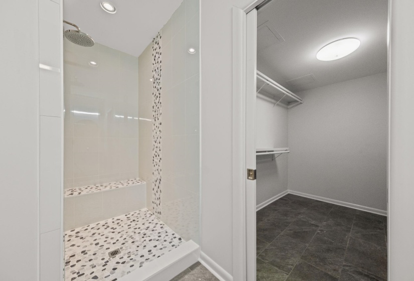 Walk-in shower with a built-in bench, pebbled flooring, rain shower head, recessed lighting, and an adjacent closet with wire shelving