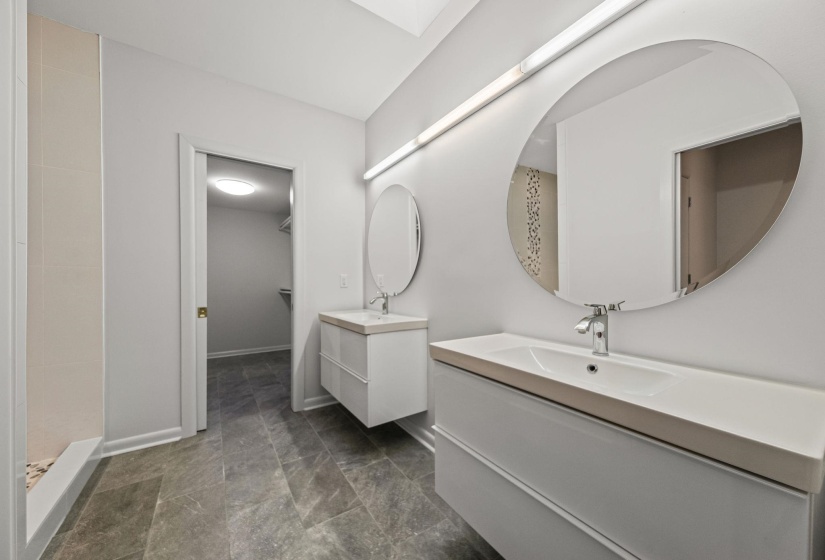 Bathroom featuring dual floating vanities with integrated sinks, contemporary chrome faucets, and circular mirrors