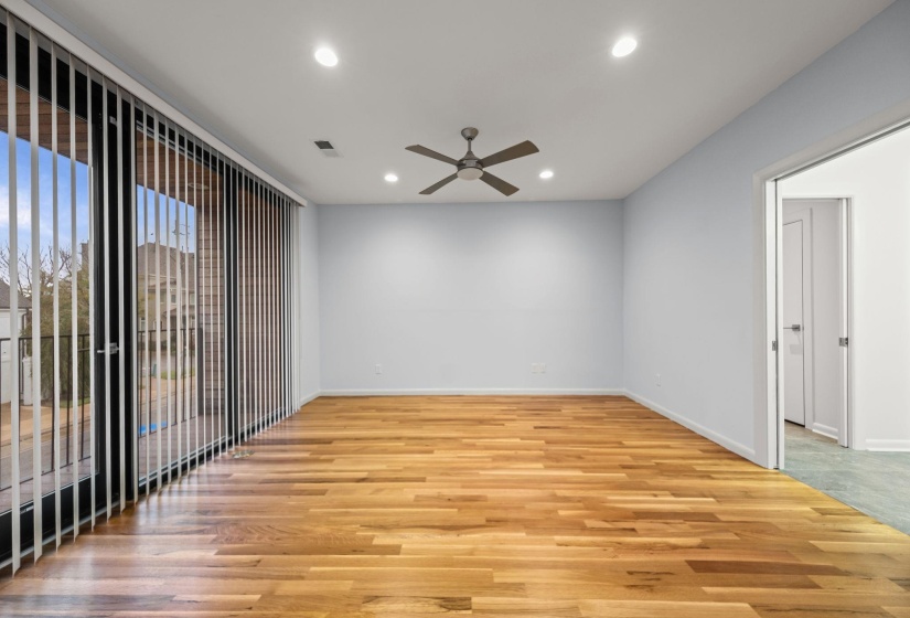 Spacious room featuring wood-finish flooring, light blue walls, and a large sliding glass door with vertical blinds