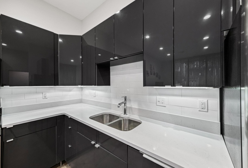 Contemporary kitchen featuring dark high-gloss cabinetry, light-toned countertops, and a white subway tile backsplash
