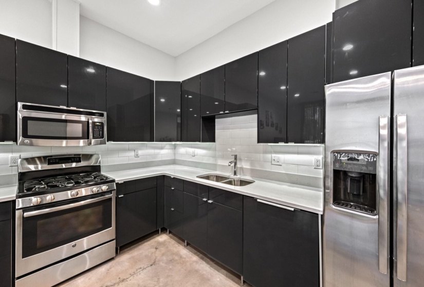 Contemporary kitchen with gloss black cabinetry, stainless steel appliances, light countertops, and a white subway tile backsplash