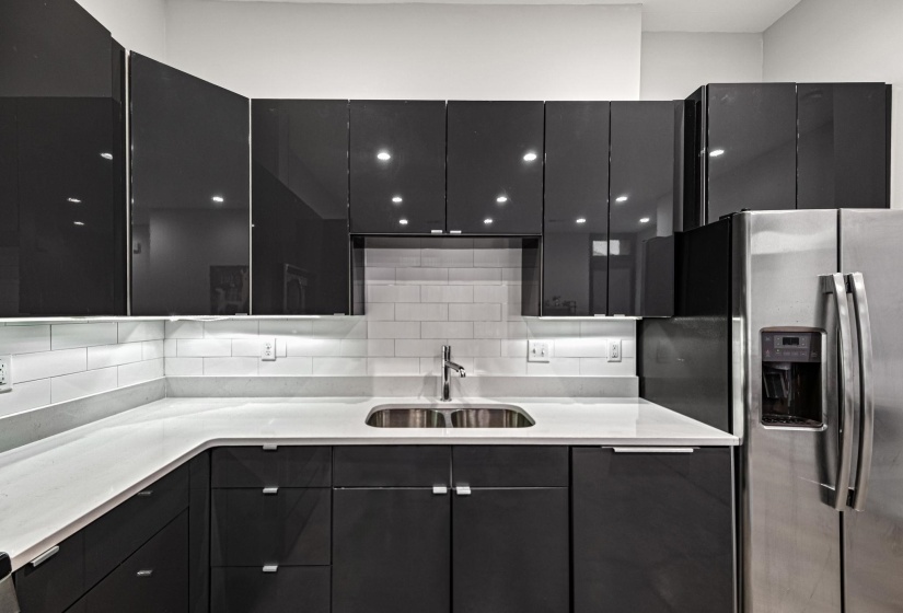 Modern kitchen featuring dark glossy cabinetry, light countertops, subway tile backsplash, and a stainless steel double-door refrigerator