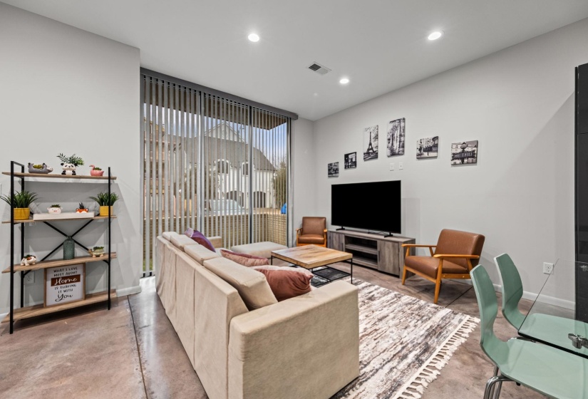 Spacious living area featuring polished concrete flooring, recessed lighting, and a large sliding glass door with vertical blinds