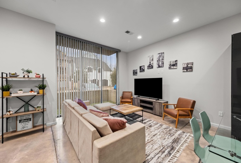 Spacious living area featuring polished concrete flooring, recessed lighting, and expansive windows with vertical blinds