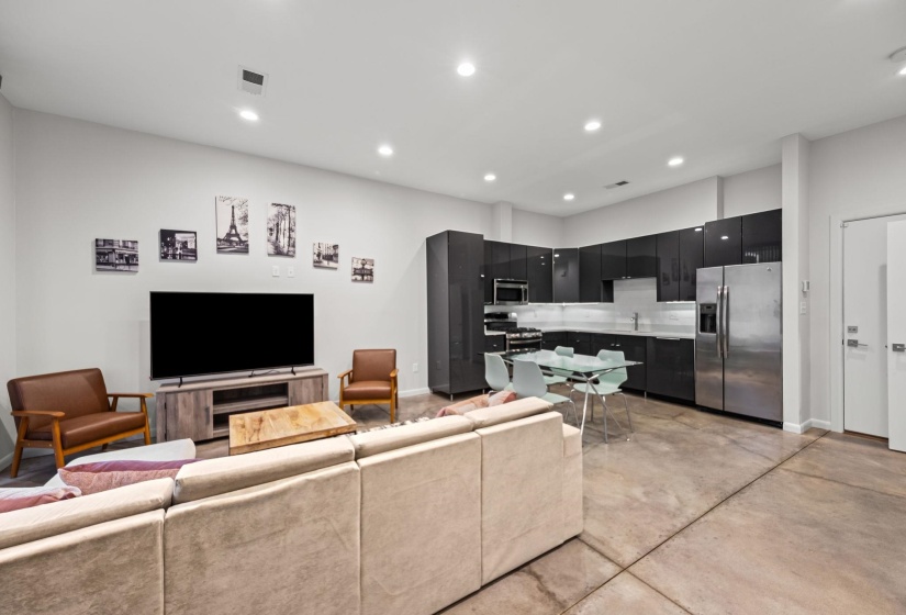 Open-concept living space featuring a contemporary kitchen with dark cabinetry, stainless steel appliances, and white countertops