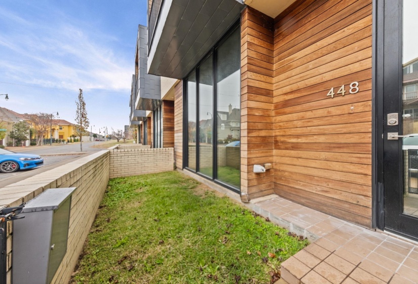Modern exterior featuring wood-finish siding, expansive windows, a brick retaining wall, and a tiled entryway