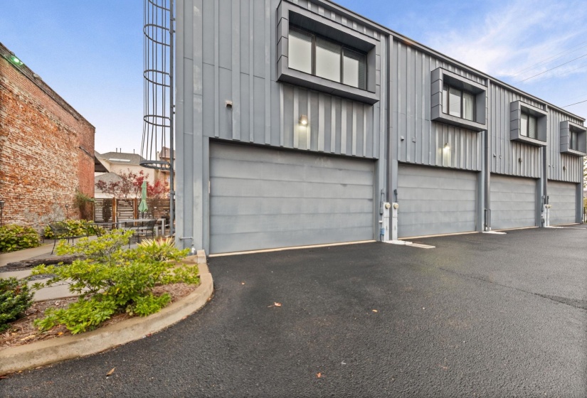 Modern industrial exterior featuring multiple overhead garage doors, vertical metal siding, and upper-level windows