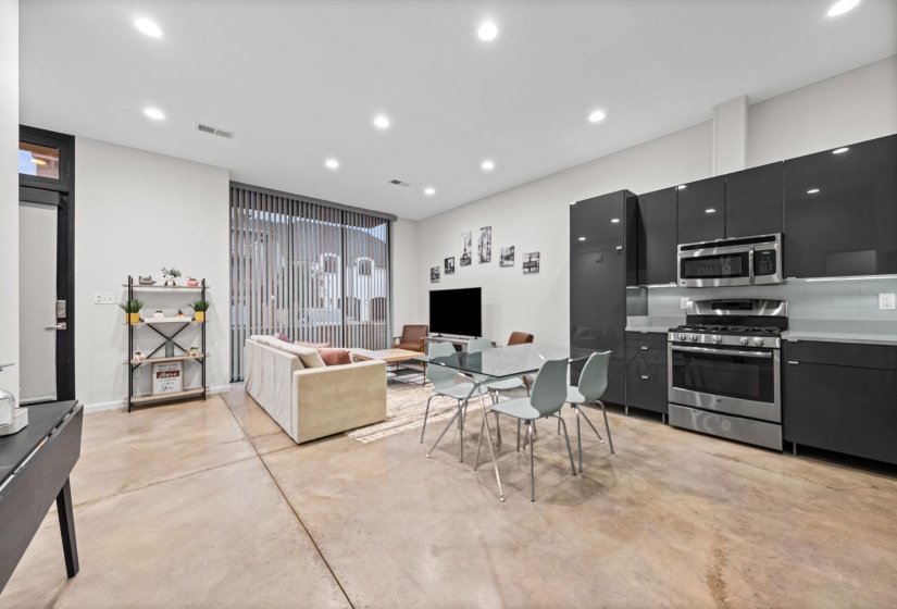 Open-concept living space featuring concrete flooring, recessed lighting, a modern kitchen with dark flat-panel cabinetry, stainless steel appliances, and a tiled backsplash