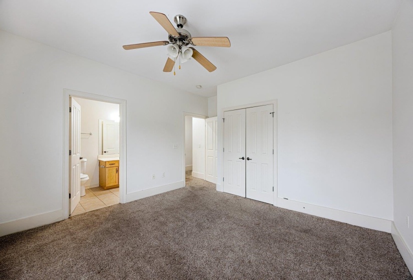 Unfurnished bedroom with light carpet, a ceiling fan, a closet, and ensuite bath