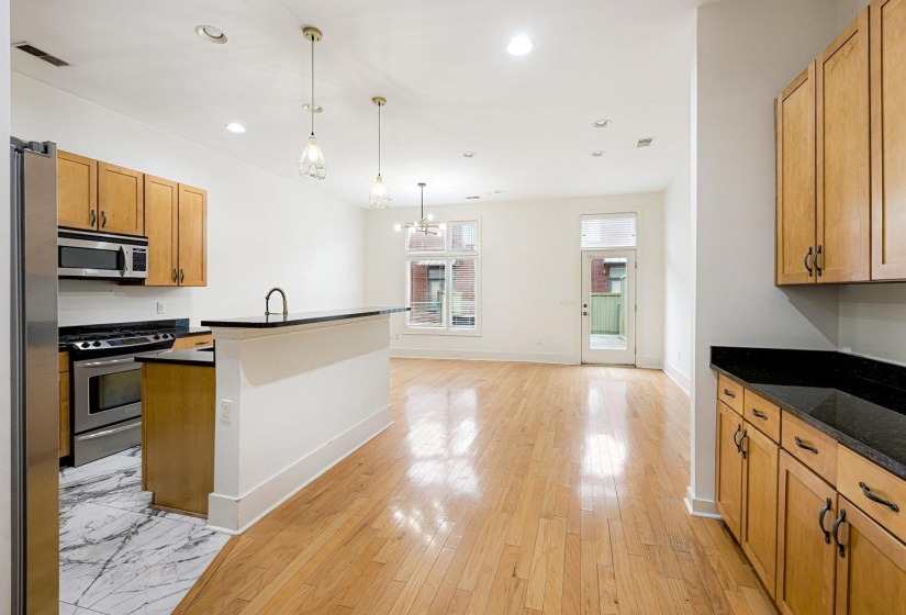 Kitchen with stainless steel appliances, light wood-style floors, dark stone countertops, wood finish cabinetry, and hanging lights