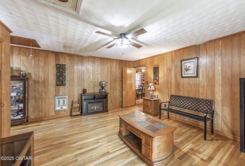 Living area featuring wood-finish flooring, wood paneling, and a ceiling fan with integrated lighting