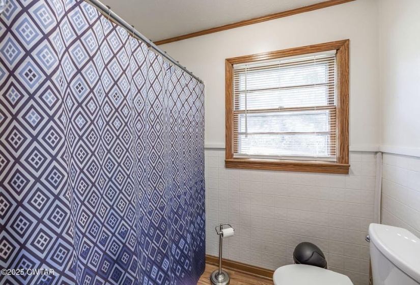 Bathroom featuring a shower with patterned curtain, wood-finish flooring, and white wall tile