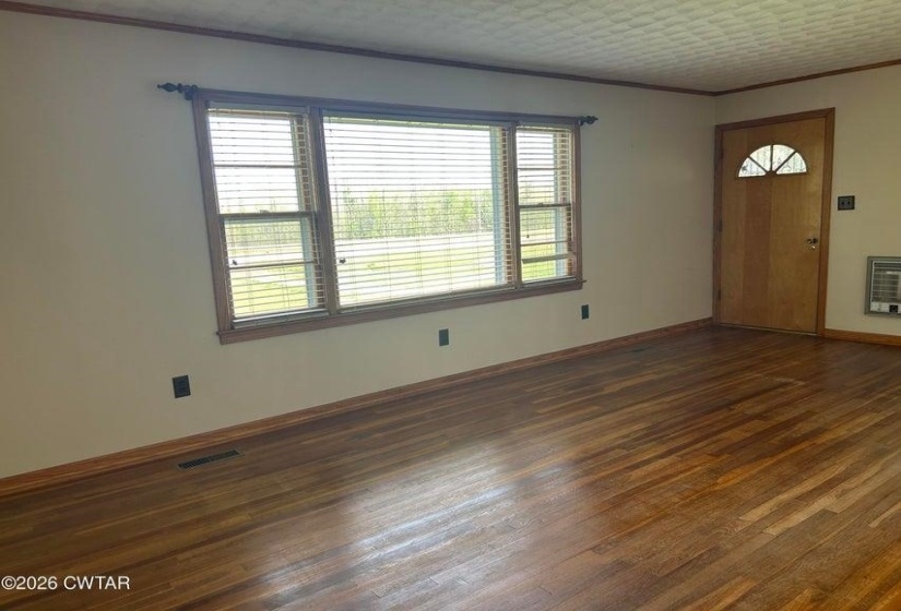 Wood-finish flooring throughout, featuring a natural wood entry door with an arched window insert, and multiple windows with blinds