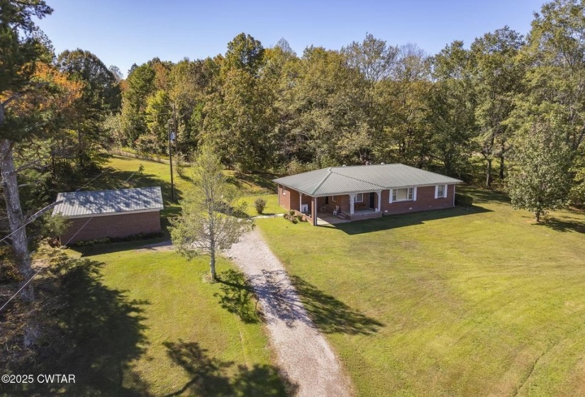 Brick ranch home featuring a covered front porch, a green metal roof, and white window frames