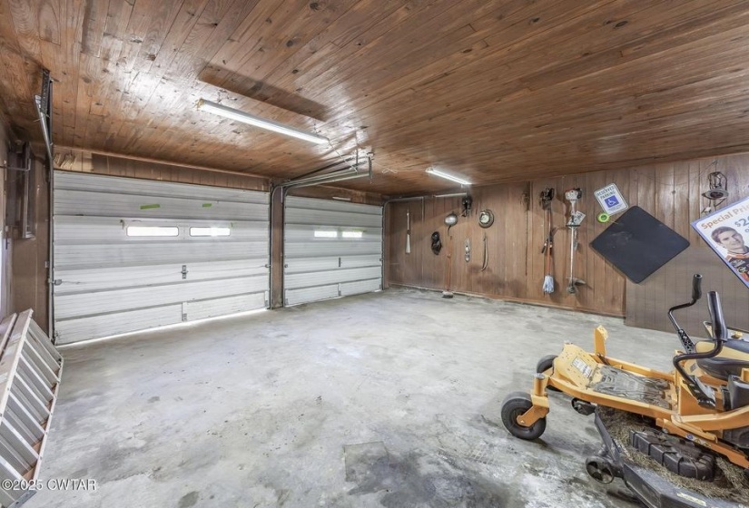 Two-car garage featuring concrete flooring, wood panel walls, wood-finish ceiling, and overhead fluorescent lighting