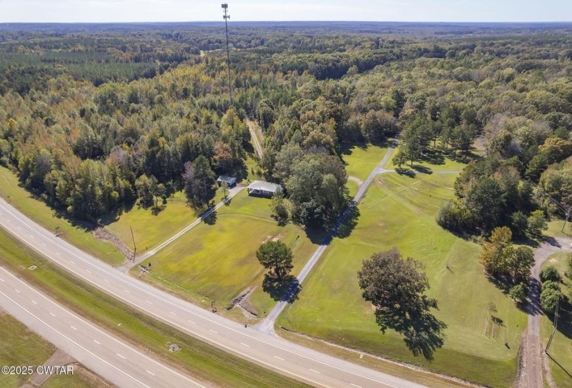 Expansive property featuring a paved multi-lane highway, verdant tree lines, and a cellular tower