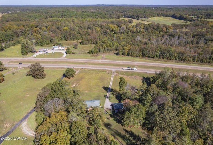 Expansive undeveloped land featuring a paved roadway, existing structures, and dense mature tree coverage